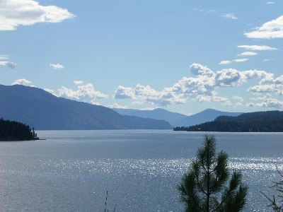 [A sparkling lake view as the sun relects off the water. The lake is huge and appears to have nooks and crannies as there are hillsides sticking out into the water. The sky has puffy white clouds in a few places.]